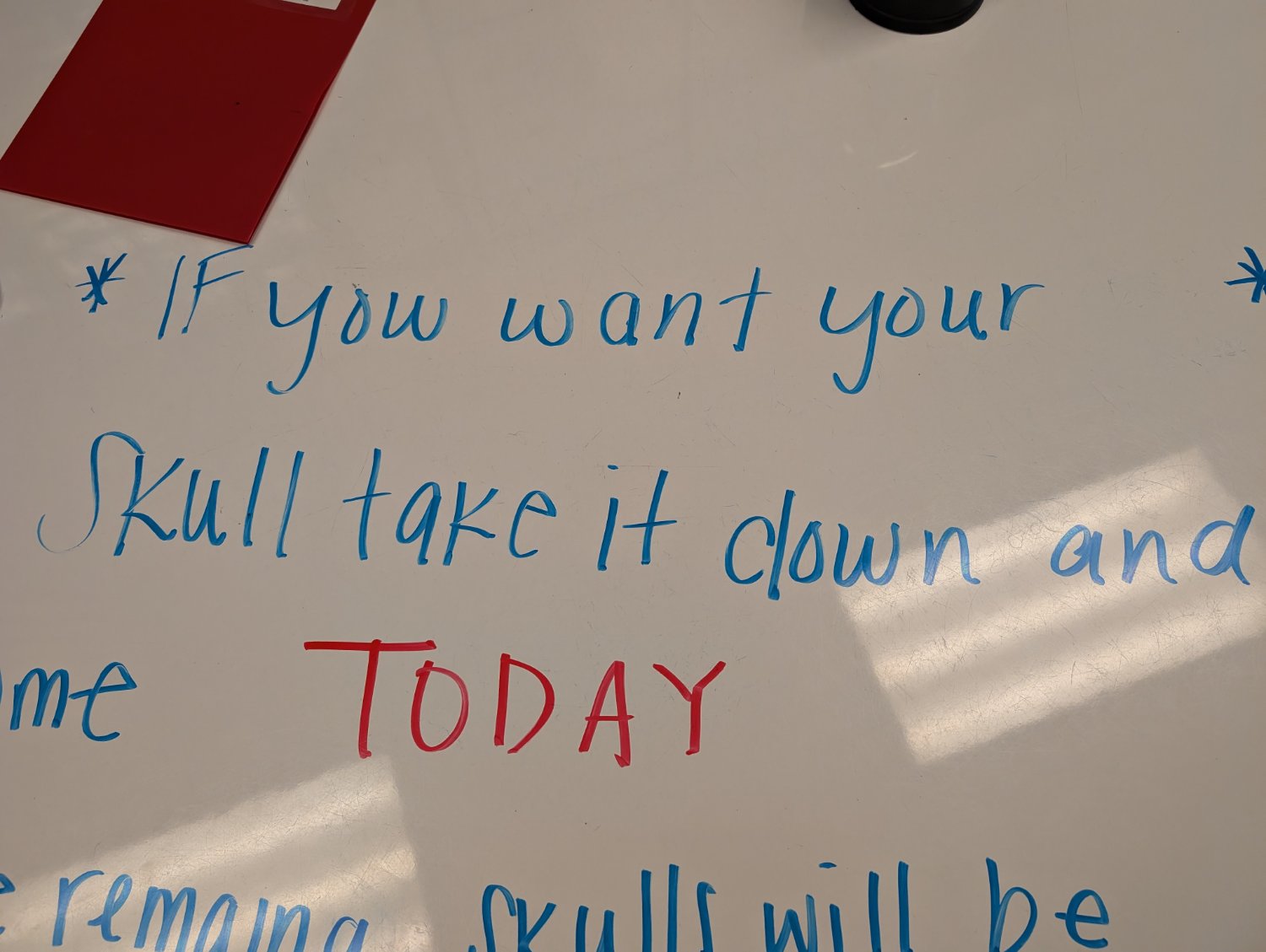 Teachers writing on a whiteboard table that says "If you want your (art project) skull take it down..." where 'down' looks like 'clown' due to the handwriting